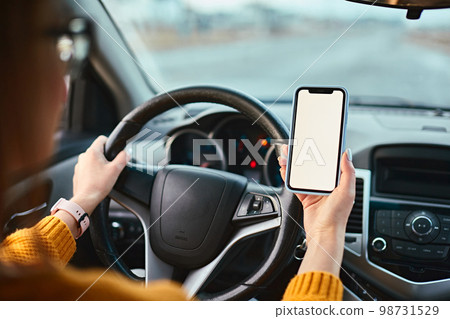 Screen blank mockup mobile phone in the hands of a woman driver in a car Screen blank mockup mobile phone in the hands of a woman driver in a car 98731529