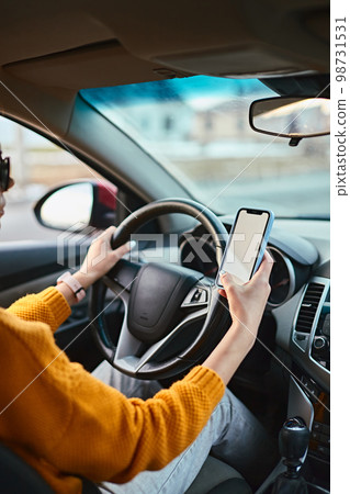Hands of unrecognizable woman driver using white screen mockup mobile phone while driving Hands of unrecognizable woman driver using white screen mockup mobile phone while driving 98731531