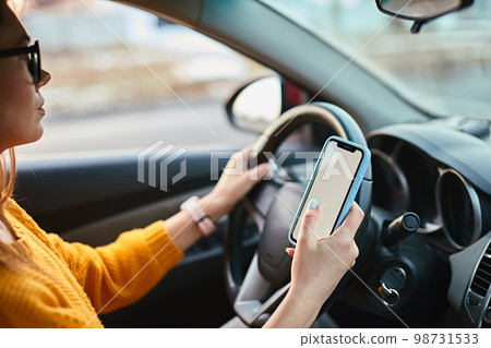 Woman driver using mobile phone screen blank mockup while driving distracted from the road Woman driver using mobile phone screen blank mockup while driving distracted from the road 98731533