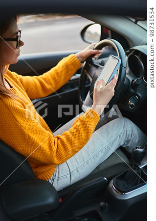 Young woman driver using mobile phone while driving car, unsafe driving Young woman driver using mobile phone while driving car, unsafe driving 98731534