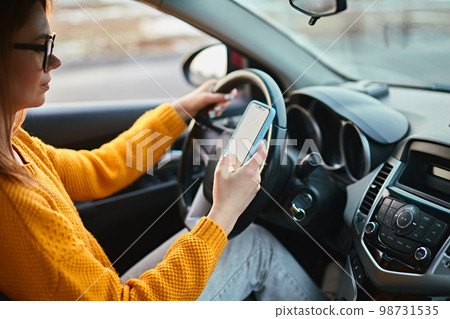 Young woman driver using mobile phone while driving car, unsafe driving 98731535