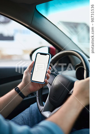 Close up Hands of unrecognizable man driver using white screen mockup mobile phone while driving Close up Hands of unrecognizable man driver using white screen mockup mobile phone while driving 98731536