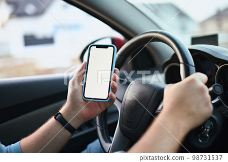Close up Hands of unrecognizable man driver using white screen mockup mobile phone while driving 98731537