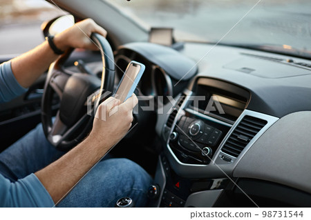 Hands of unrecognizable man driver using mobile phone while driving 98731544