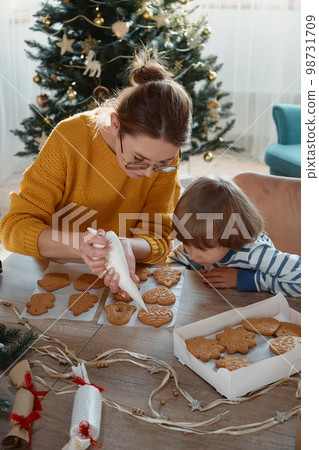 Mother and child decorating Christmas gingerbread cookies with icing sugar together Mother and child decorating Christmas gingerbread cookies with icing sugar together 98731709