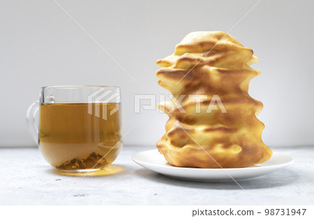 Sakotis ,sekacz, baumkuchen is traditional spit cake in lithuanian, polish, german, belarusian cuisine made of butter, eggs, flour, sugar cooked on rotating spit over open fire. Cup of tea. Horizontal 98731947
