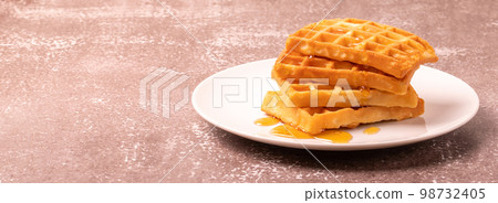 Delicious Belgian waffles with honey served on white plate and brown background, rustic concept, space for text 98732405