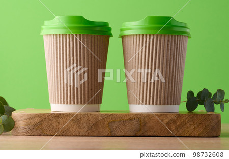 Paper brown cups with a plastic green lid for coffee and tea on a green background Paper brown cups with a plastic green lid for coffee and tea on a green background 98732608