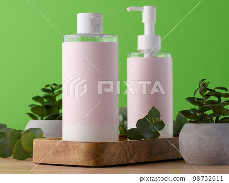 Two bottles for cosmetics with a pink paper label on a green background. Bottle for tonic, gel Two bottles for cosmetics with a pink paper label on a green background. Bottle for tonic, gel 98732611