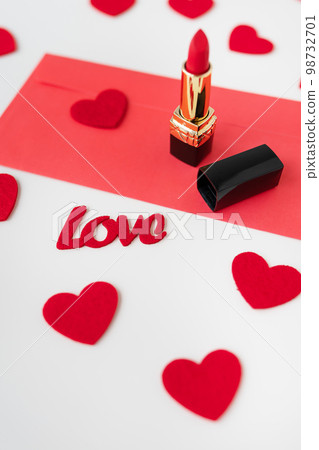 A red envelope with red lipstick on a background of small red hearts. The concept of the holiday February 14, St. Valentine's Day. A red envelope with red lipstick on a background of small red hearts. The concept of the holiday February 14, St. Valentine's Day. 98732701