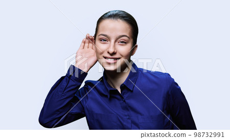 Young female holding hand near ear, listening attentively, on white background 98732991