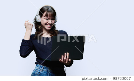 Happy young female in headphones looking at laptop yes sign, on white background Happy young female in headphones looking at laptop yes sign, on white background 98733007