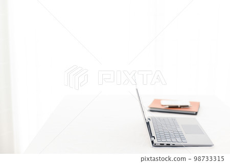 A laptop, a smartphone, and a system notebook (keyboard focus) on a white desk A laptop, a smartphone, and a system notebook (keyboard focus) on a white desk 98733315