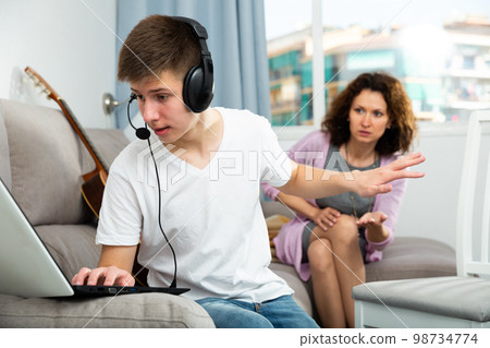 Teenager with laptop gesturing enough to mother Teenager with laptop gesturing enough to mother 98734774