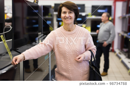 Portrait of a smiling woman standing in the department with televisions Portrait of a smiling woman standing in the department with televisions 98734788