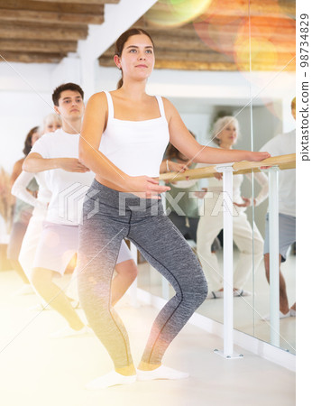Young concentrated woman rehearsing ballet dance with other dancers in training room. Young concentrated woman rehearsing ballet dance with other dancers in training room. 98734829