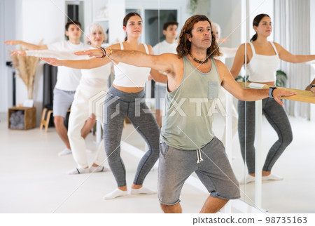 Dancer man exercise near the ballet barre at a group training session in the dance studio. Dancer man exercise near the ballet barre at a group training session in the dance studio. 98735163