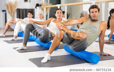 Active vigorous man performs exercises with a pilates roller while on a mat in the hall of a modern fitness studio. Active vigorous man performs exercises with a pilates roller while on a mat in the hall of a modern fitness studio. 98735216