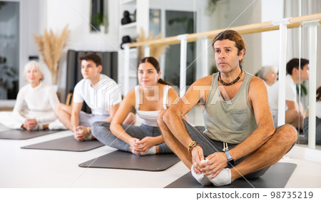 Middle-aged man practicing pilates on gray mat in gym room 98735219