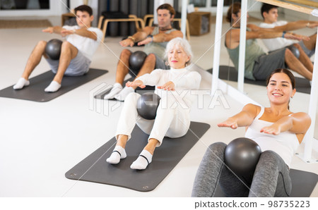 Sporty energetic males and females doing exercises with pilates ball during group training at gym. Fitness concept. 98735223