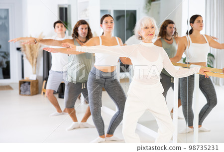Аged woman choreographer demonstrates ballet stances to students in a modern dance studio. Аged woman choreographer demonstrates ballet stances to students in a modern dance studio. 98735231