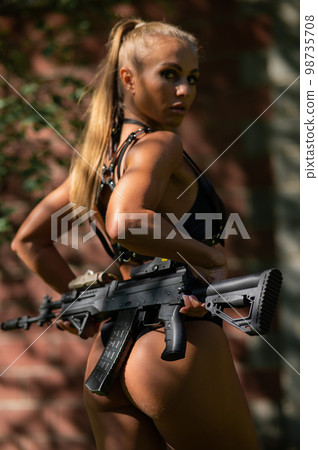 Caucasian woman in bikini with machine gun outdoors. 98735708
