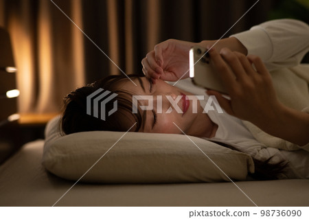 A woman who operates a smartphone while rubbing her eyes in a bed/bedroom 98736090