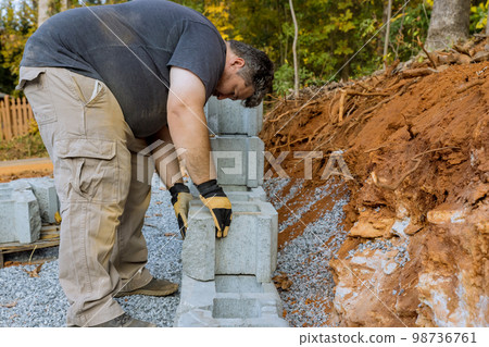 On construction site of construction worker was installing concrete block for retaining wall next to new house 98736761