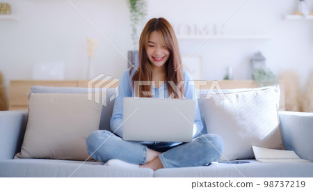 Young asian woman using laptop while seated on couch at home 98737219