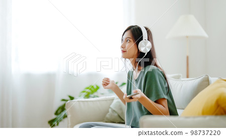 Young asian woman listening to music on couch in living room at home Young asian woman listening to music on couch in living room at home 98737220