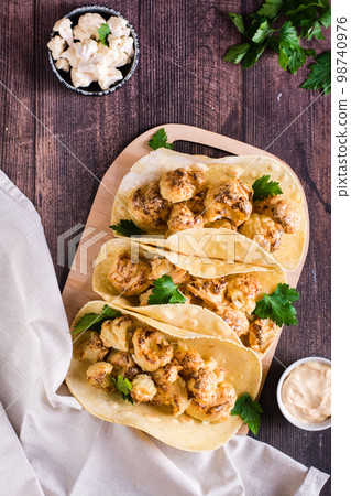 Grilled cauliflower tacos with herbs on a board on the table. Vegetarian food. Top and vertical view Grilled cauliflower tacos with herbs on a board on the table. Vegetarian food. Top and vertical view 98740976