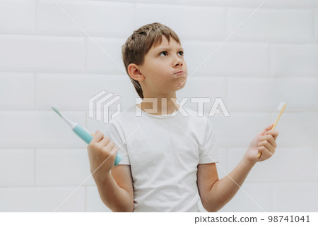 cute 8 years old boy holding bamboo and electric tooth brush making choice cute 8 years old boy holding bamboo and electric tooth brush making choice 98741041