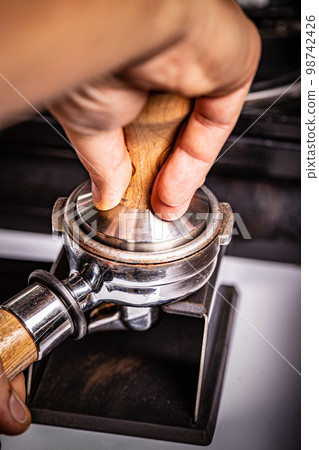 Barista presses ground coffee 98742426