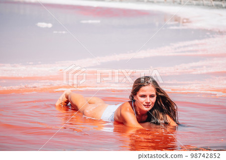 Young woman with long hair in pink salty lake with crystals of salt. Extremely salty pink lake, colored by microalgae with crystalline salt depositions. Spa, beauty and health care concept. Young woman with long hair in pink salty lake with crystals of salt. Extremely salty pink lake, colored by microalgae with crystalline salt depositions. Spa, beauty and health care concept. 98742852