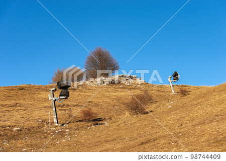 Snow Cannons or Snowmaking System on a Brown Ski Slope - Italy 98744409