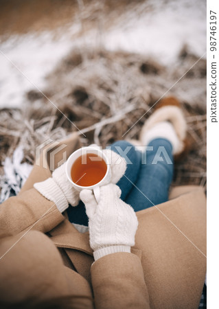 Unrecognizable woman in white woolen mittens holding cup of tea enjoying winter frozen nature Unrecognizable woman in white woolen mittens holding cup of tea enjoying winter frozen nature 98746197