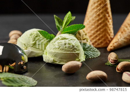 Tasty pistachio ice cream decorated with fresh mint and served on a stone slate over a black background. Tasty pistachio ice cream decorated with fresh mint and served on a stone slate over a black background. 98747815