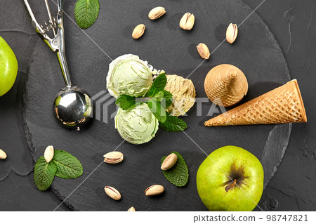 Delicious pistachio and chocolate ice cream decorated with fresh mint and served on a stone slate over a black background. 98747821