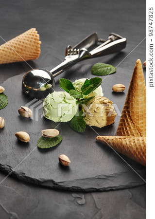 Delicious pistachio and chocolate ice cream decorated with fresh mint and served on a stone slate over a black background. 98747828