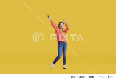 Cheerful joyful teen girl in casual clothes having fun and dancing on isolated on yellow background. 98749100