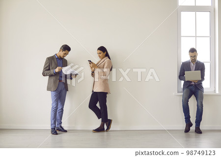 Full-size photo of partners standing near wall in spacious bright room. Full-size photo of partners standing near wall in spacious bright room. 98749123