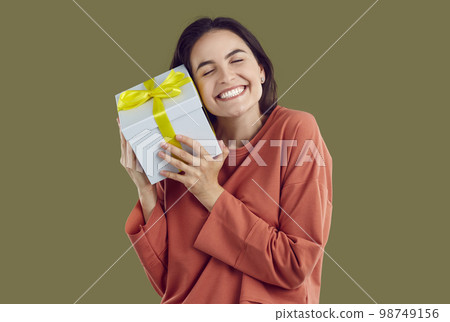 Smiling brunette woman in red sweatshirt is hugging a present with closed eyes on khaki background. 98749156