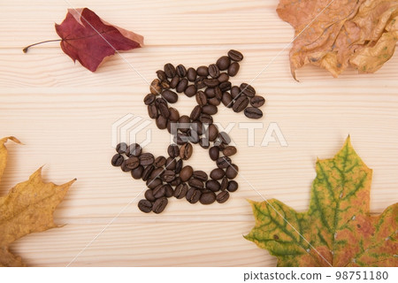 Dollar sign. A sign denoting American money. A dollar made from roasted coffee beans lies on a wooden tabletop. Nearby are several autumn leaves 98751180