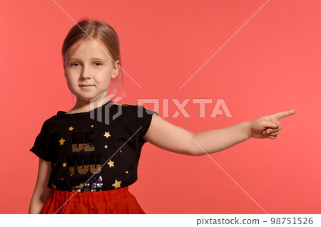 Close-up shot of a charming blonde little lady in a combined dress posing against a pink background. 98751526