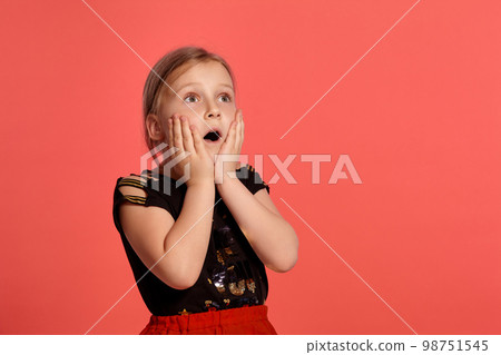 Close-up shot of a charming blonde little lady in a combined dress posing against a pink background. 98751545