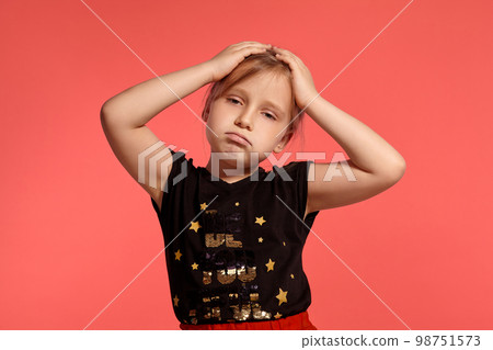 Close-up shot of a charming blonde little lady in a combined dress posing against a pink background. 98751573