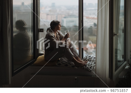 Young unhappy woman with cancer sitting in a window and looking at view. 98751857