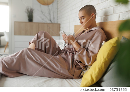 Young woman with cancer siting at home and scrolling her phone. 98751863