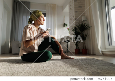 Young woman with cancer siting at home and scrolling her phone. 98751907