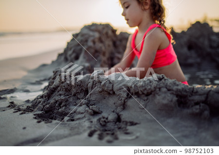 Little girl playing on the beach, digging hole in sand. 98752103